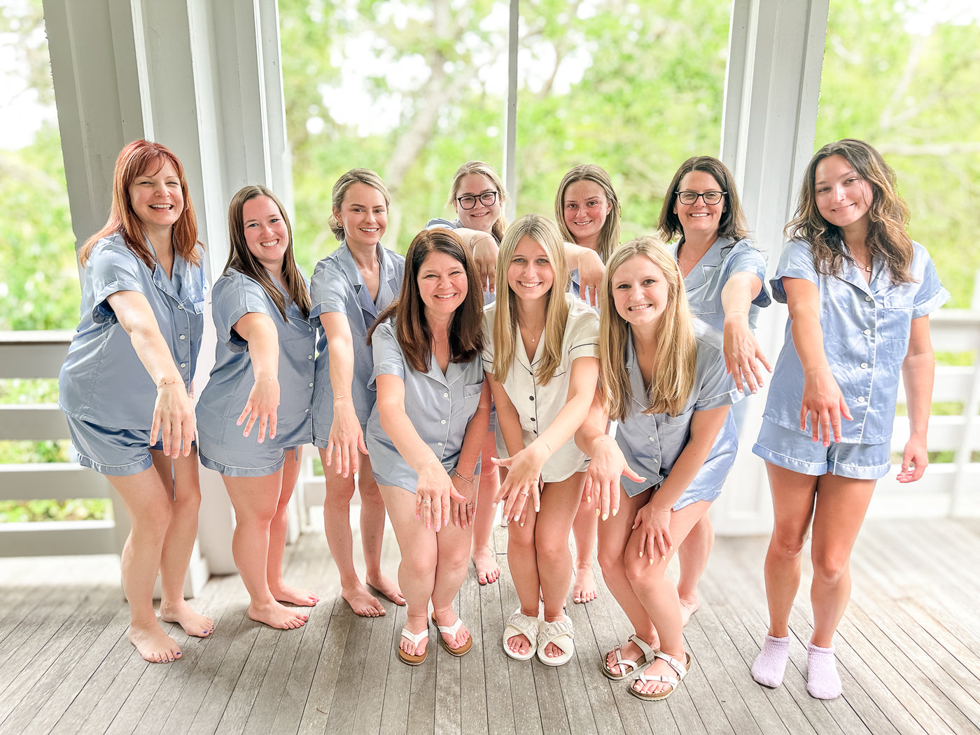 Group of women posing together on a wooden deck at a bachelorette party with a blurred green outdoor background showing off their new permanent jewelry bracelets in Isle of Palms, SC